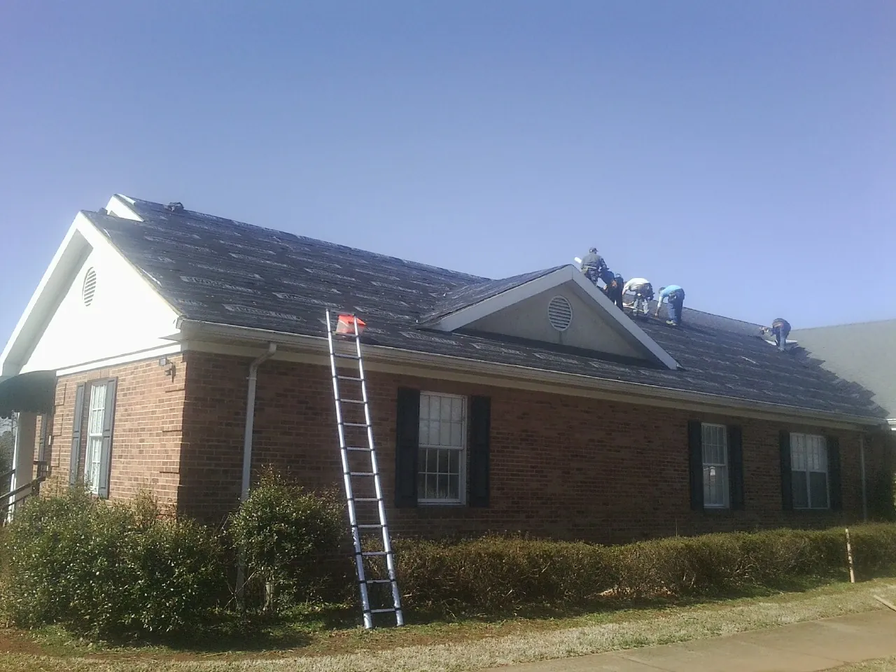 Crew tearing shingles off a brick ranch roof with a ladder set — Emergency Roof Repair work by our crew in Bolckow