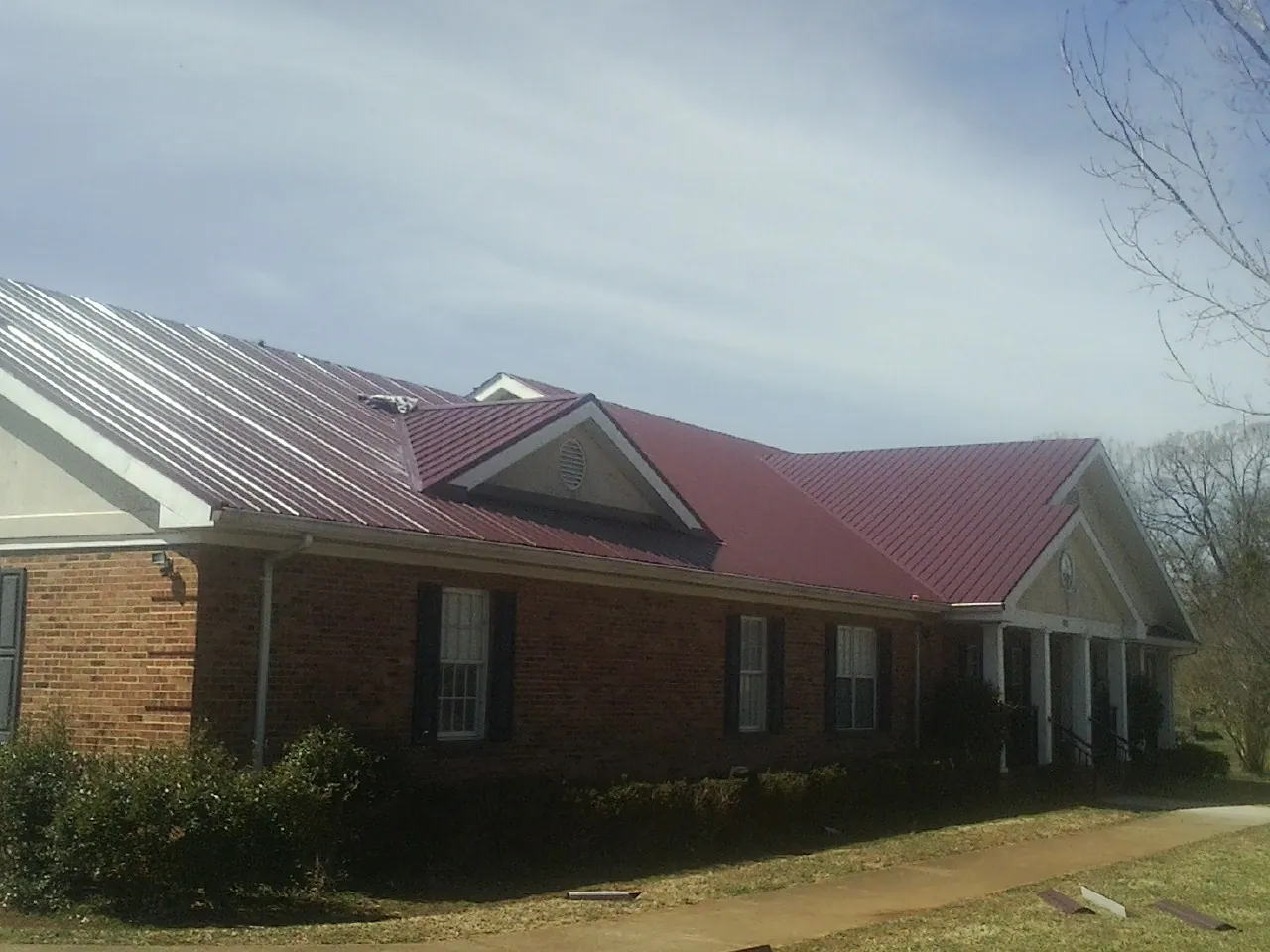 Red metal roof with gabled entries on a long brick building, from a Hail Damage Roof Repair job in Bolckow