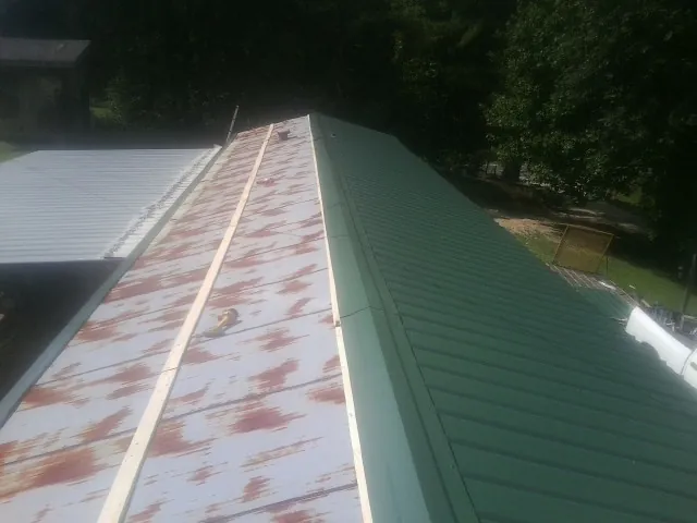 Old rusted panels beside newly installed green metal roofing — Wind Damage Roof Repair by Roofing Brothers in Bolckow