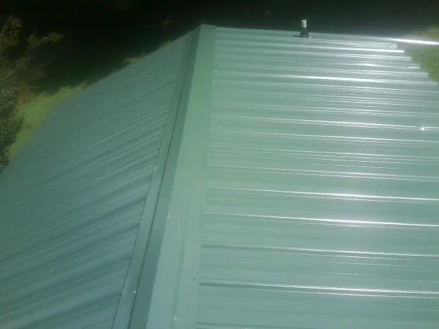 New green metal panels meeting at the ridge of a roof — Flat Roof Repair work by our crew in Bolckow