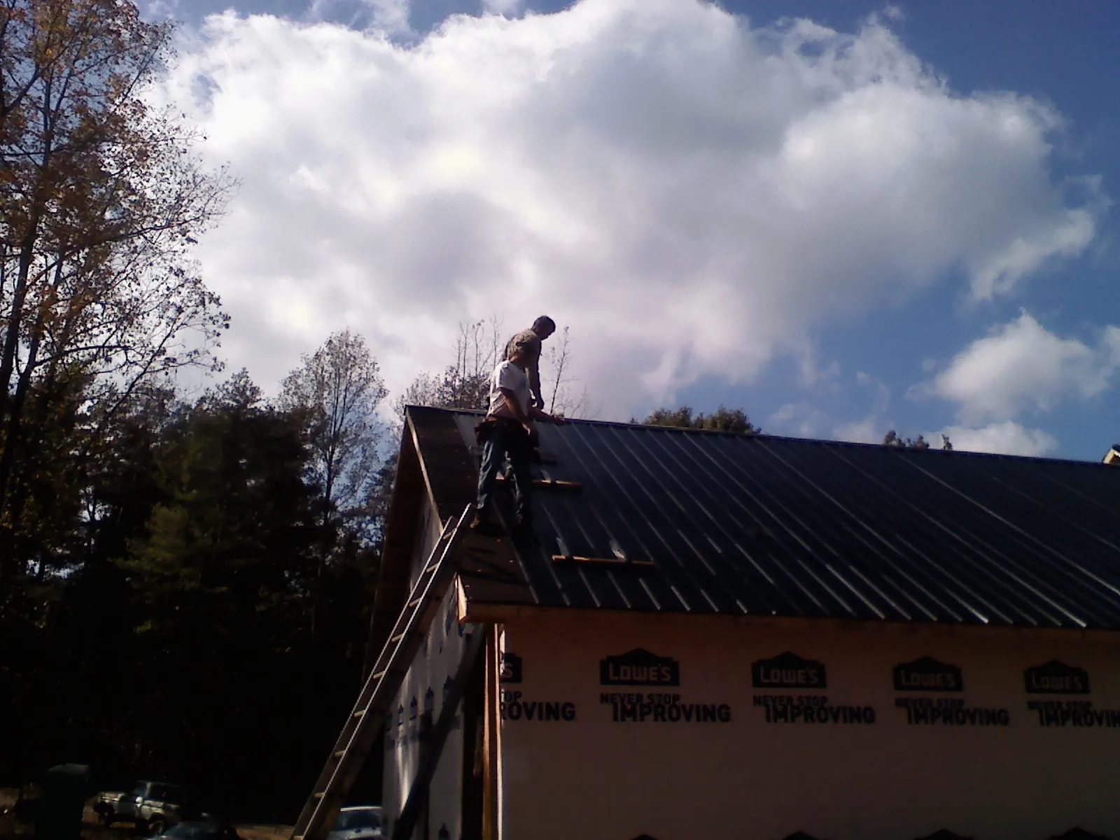 Roofer fastening dark metal panels high against a cloudy sky, from a Roof Inspection job in Bolckow