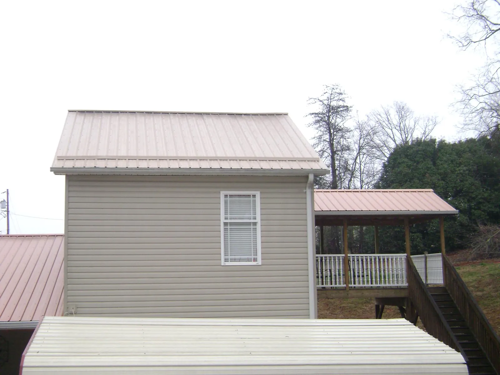 Tan metal roofs on a two story addition and attached porch, from a Roof Replacement job in Bolckow